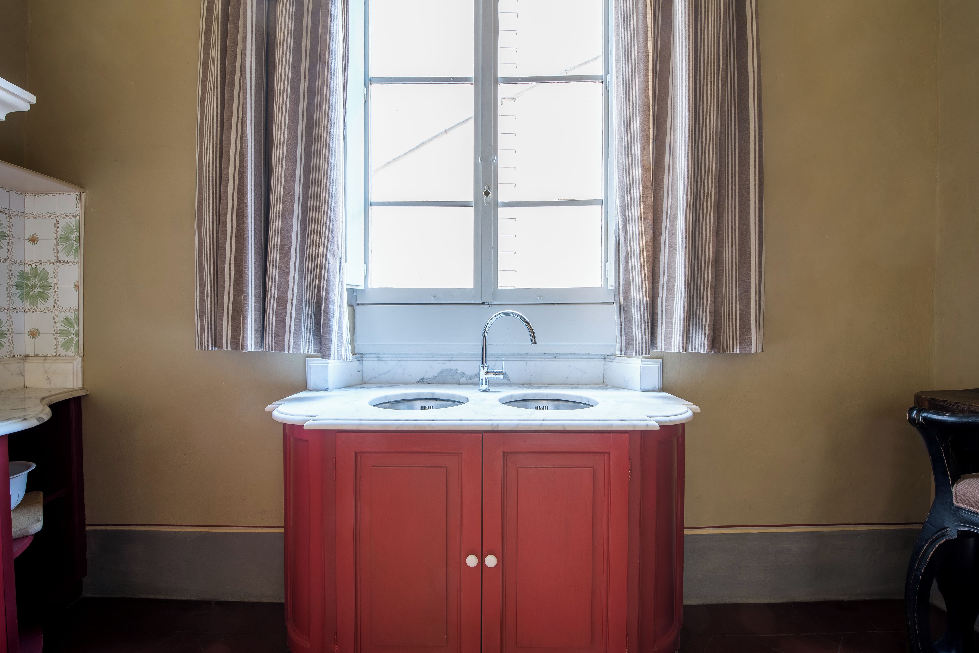 Un baño con lavamanos, ventana con cortinas y pared de azulejos.