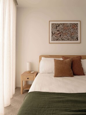 A neatly made bed with a green blanket, a wooden nightstand with a lamp, and a framed abstract art piece on the wall. - The Lagoon, Main Beach (Main Beach)