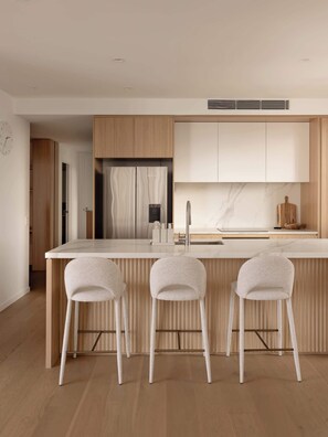 A modern kitchen with a central island, three bar stools, wooden cabinetry, and a marble backsplash. - The Lagoon, Main Beach (Main Beach)