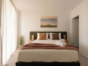Une chambre à coucher avec un grand lit, une tête de lit, une table de chevet, une plante en pot et un tableau accroché au mur.