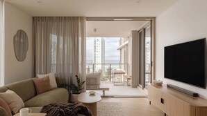 A modern living room with a sofa, a coffee table, a TV, and a balcony with a view of buildings. - The Lagoon, Main Beach (Main Beach)