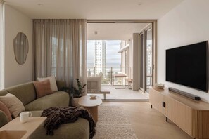 A modern living room with a sofa, a coffee table, a TV, and a balcony with a view of buildings. - The Lagoon, Main Beach (Main Beach)