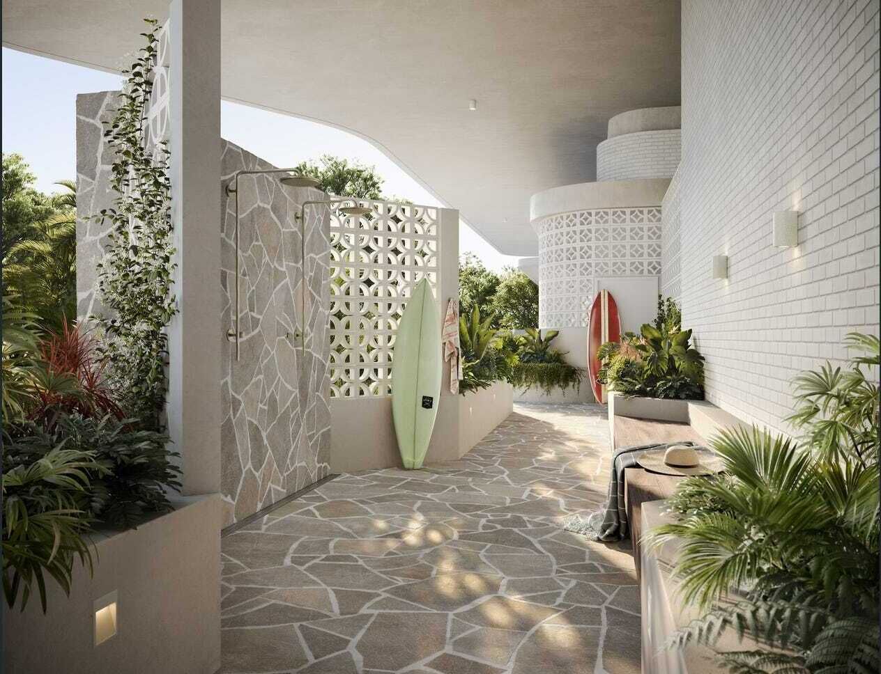 Un espace extérieur moderne avec un sol en pierre, des murs blancs et une planche de surf appuyée contre un mur blanc.