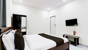 A hotel room with a bed, a bedside table, a mirror, a wall-mounted TV, and a door. - Super Collection O Vanasthalipuram (Hyderabad)