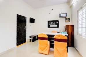 A room with a black-framed television, a sign indicating a company-serviced collection, a small table with a chair, and a window with bars. - Super Collection O Vanasthalipuram (Hyderabad)