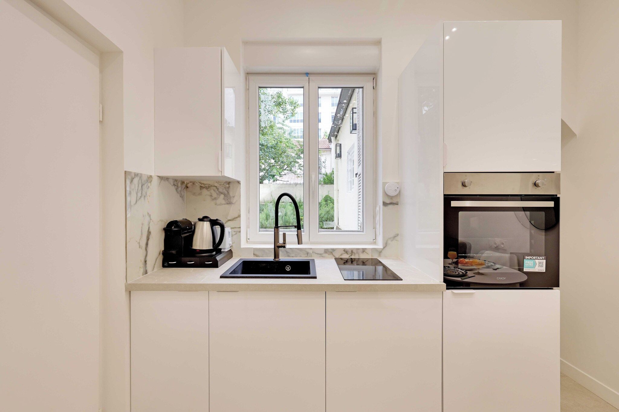 A modern kitchen with a built-in oven, a window with a view of the outside, and a marble backsplash.
