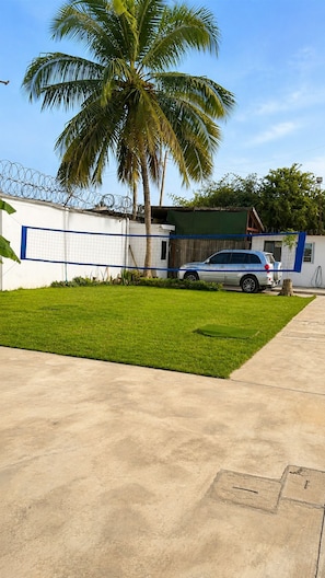 Un barrio residencial con entrada pavimentada, césped, una palmera y un coche estacionado.