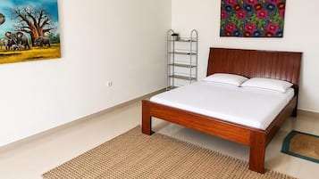 Quarto com cama de madeira, escada de metal, tapete tecido e duas obras de arte na parede.