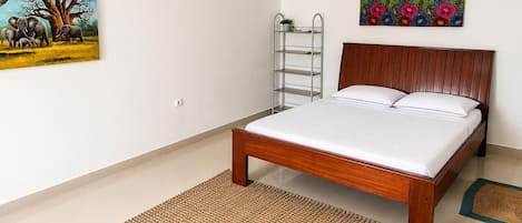 Une chambre avec un lit en bois, une échelle en métal, un tapis tissé et deux œuvres d’art murales.