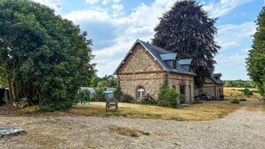 Un bâtiment en pierre doté d’un toit en pente, entouré d’arbres et bordé d’une allée gravillonnée.