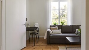 A room with a dark grey sofa, a small table with a fan, a chair, and a window with curtains. - Peaceful Stay near Uppsala - Near Forests & Nature (Österbybruk)