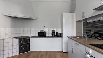 Kompakti keittiö, jossa on valkoiset kaapit, musta työtaso, mikroaaltouuni, kahvinkeitin ja liesi.