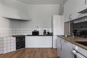 A compact kitchen with white cabinets, a black countertop, a microwave, a coffee maker, and a stove.
