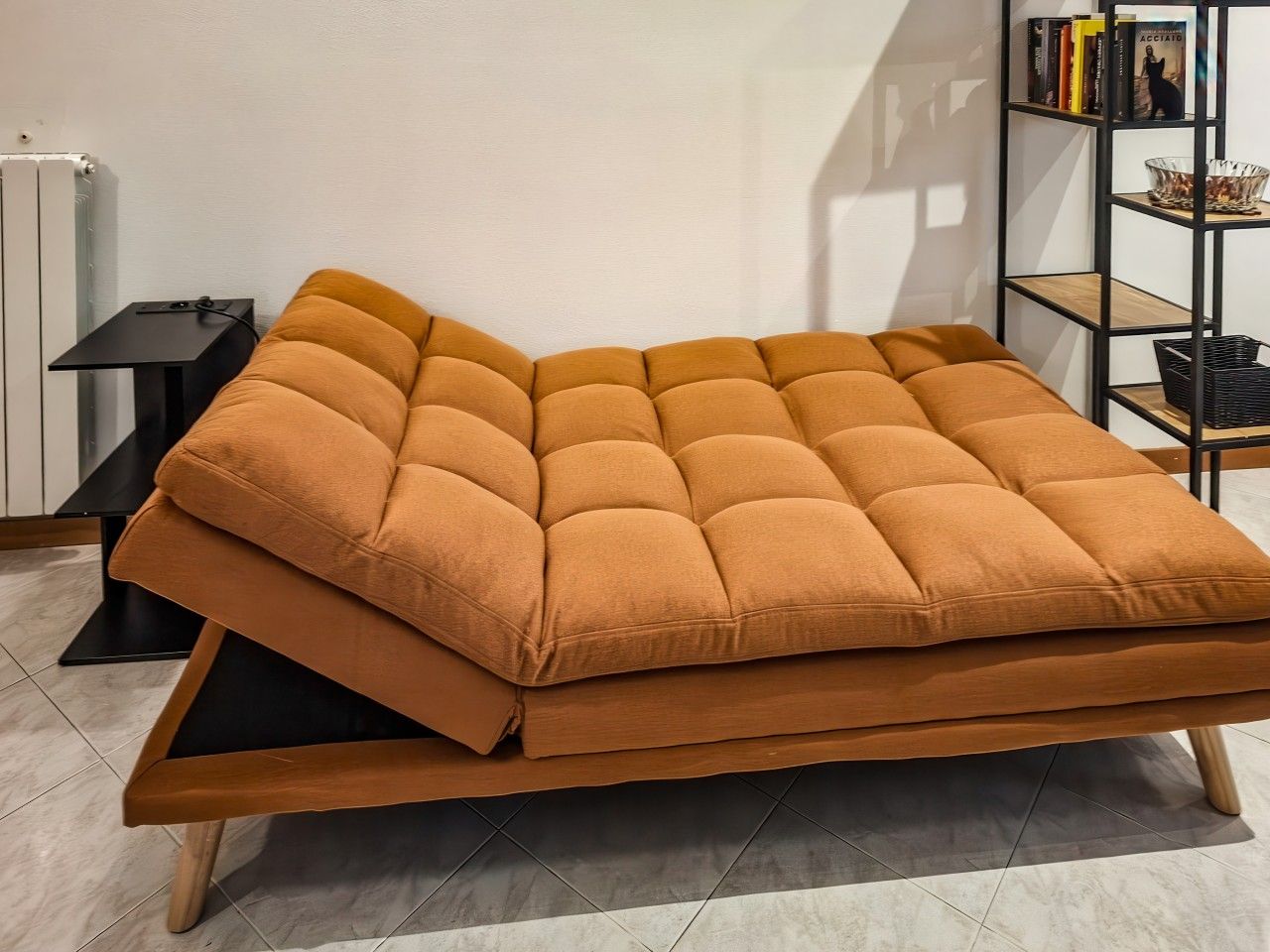 Un sofá con estructura de madera y un cojín, sobre un piso de baldosas.