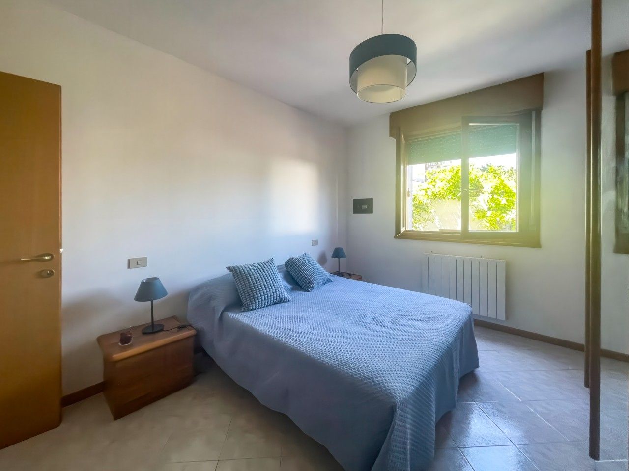 Ein Schlafzimmer mit einem Bett, Nachttischlampen, einem Fenster und einer Heizung.