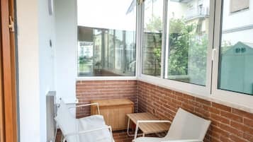 Ein kleiner Balkon mit zwei weißen Stühlen, einem Korbstuhl-Tisch und Blick auf benachbarte Gebäude.
