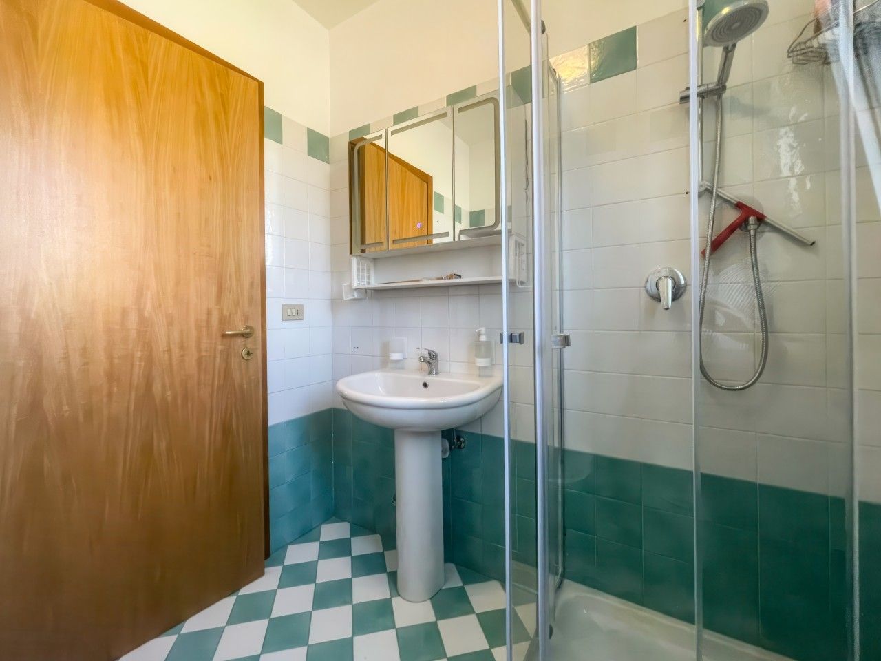 Un baño con puerta de madera, un lavabo blanco, un espejo y una cabina de ducha.