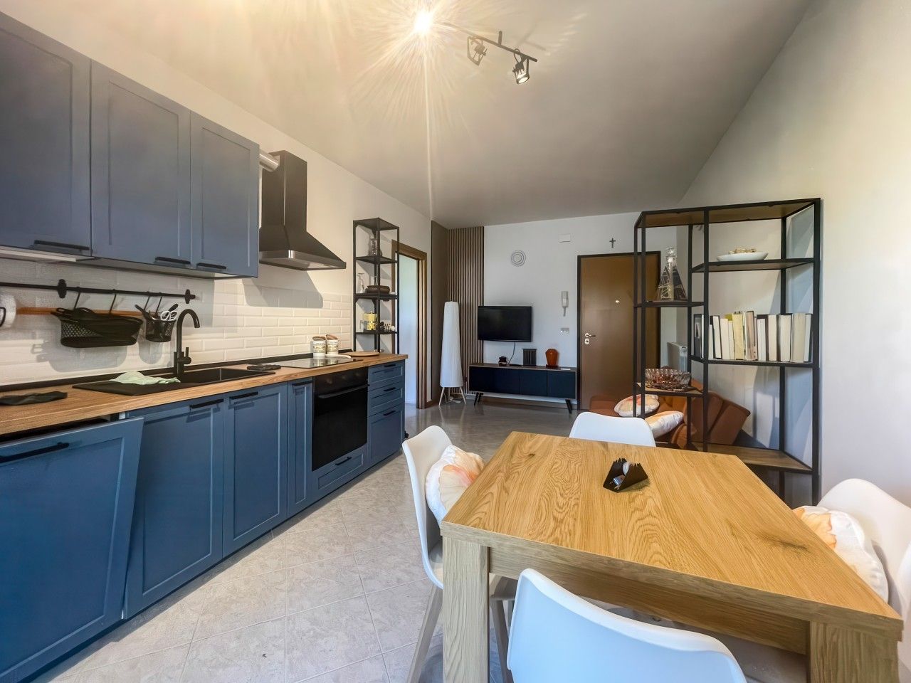 A modern kitchen with blue cabinets, a wooden dining table, and white chairs.