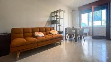 Ein modernes Wohnzimmer mit einer Couch, einem Esstisch mit Stühlen und einem großen Fenster.