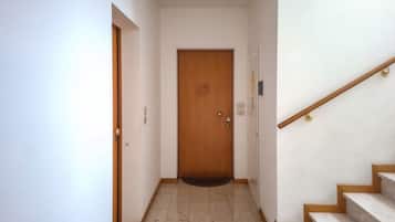 A hallway with a wooden door, a staircase with wooden handrails, and a tiled floor.
