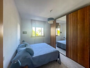Una camera da letto con un letto, un comodino, una lampada, una finestra e uno specchio.