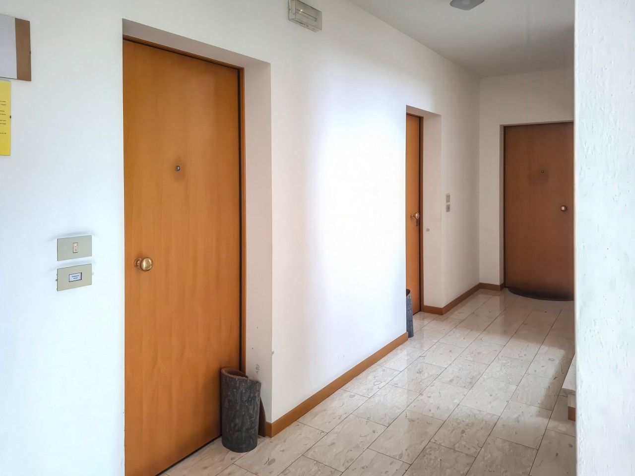 Ein Korridor mit Holztüren, einem Mülleimer und einem Lichtschalter an der Wand.