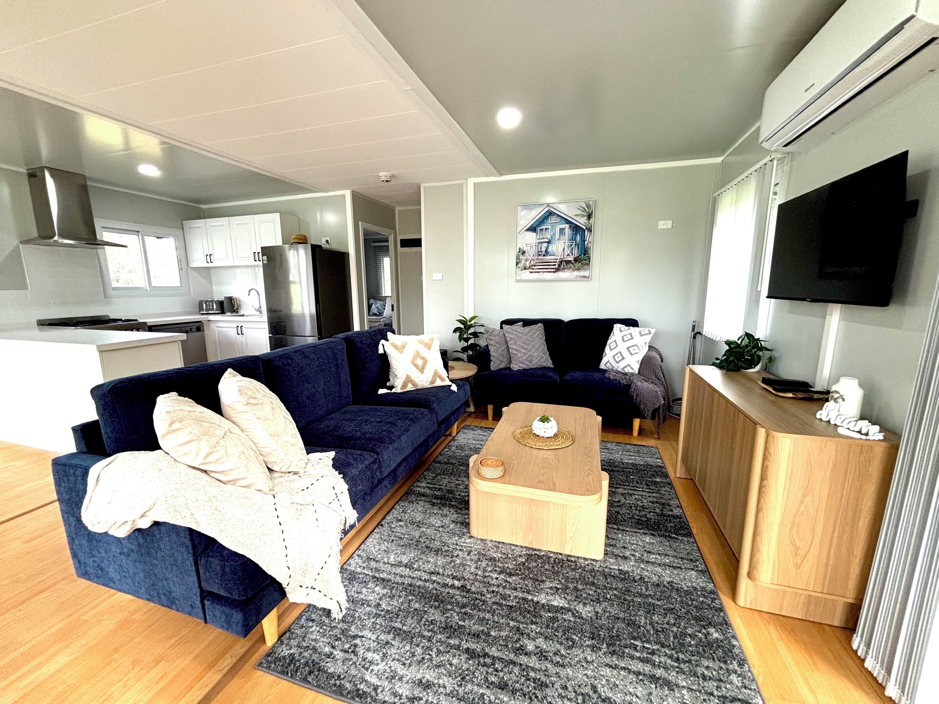 A modern living room with a blue sofa, a wooden coffee table, and a TV mounted on the wall.