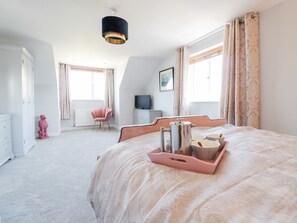 Ein Schlafzimmer mit Bett, Kommode, Sessel, Fernseher und einem Fenster mit Vorhängen.