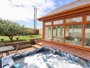 A hot tub in a backyard with a brick wall and a window overlooking a lawn. - Ger Y Mor (Cemaes Bay)