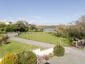 A coastal property with a paved driveway leading to a grassy area, a white wall, and a view of the sea. - Ger Y Mor (Cemaes Bay)