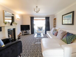 A living room with a fireplace, a sofa, a television, and a patterned floor. - Ger Y Mor (Cemaes Bay)