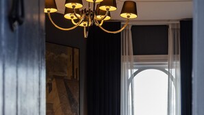 Ein Hotelzimmer mit einem Bett, einem Nachttisch, einer Lampe, einer Vase mit Blumen und Blick durch ein großes Fenster.