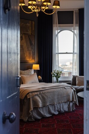 A hotel room with a bed, a nightstand, a lamp, a vase with flowers, and a view through a large window. - Wahroonga on Bourke (Launceston)