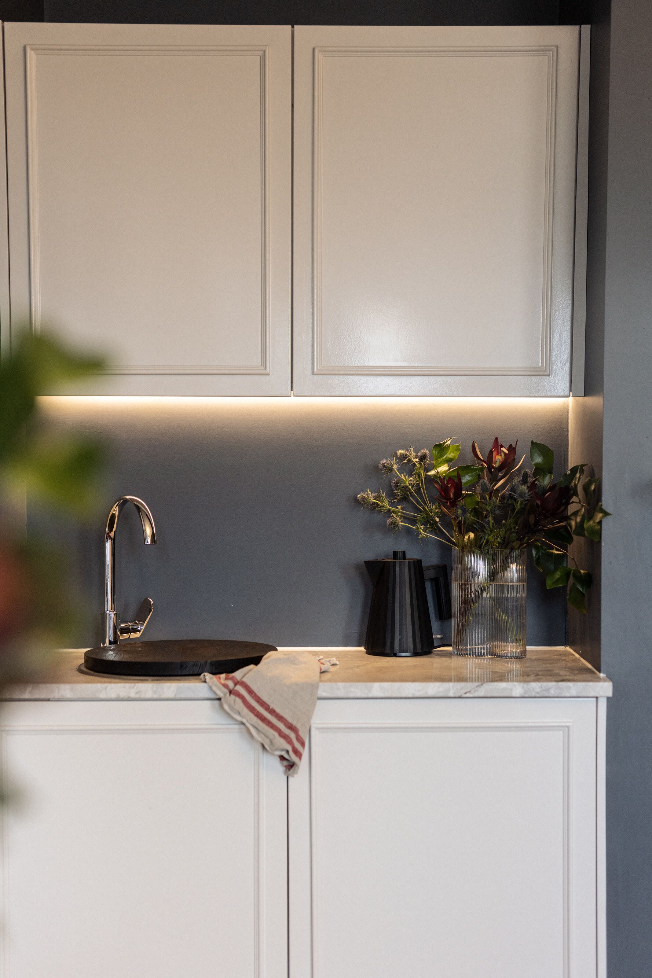 A kitchen with white cabinets, a stainless steel faucet, a black countertop, and a vase with flowers.