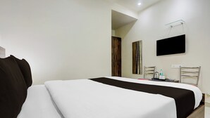 Ein Hotelzimmer mit einem Bett, einem an der Wand befestigten Flachbildfernseher, einem Sessel und einem kleinen Tisch mit einer Flasche und Gläsern.