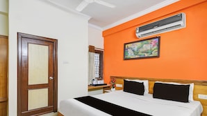 Habitación de hotel con cama, ventana con cortinas, equipo de aire acondicionado y un cuadro en la pared.