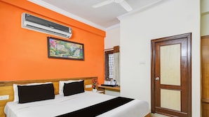 Habitación de hotel con cama, aire acondicionado, un cuadro, ventana con cortinas y puerta de madera.