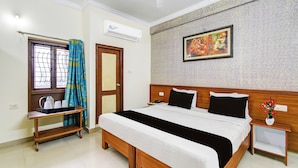 Habitación de hotel con cama, mesita de noche, cortinas en la ventana, aire acondicionado y un cuadro colgado en la pared.