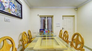 Un comedor con una mesa de vidrio rodeada de sillas de madera, una obra de arte enmarcada en la pared y una puerta con ventanal.