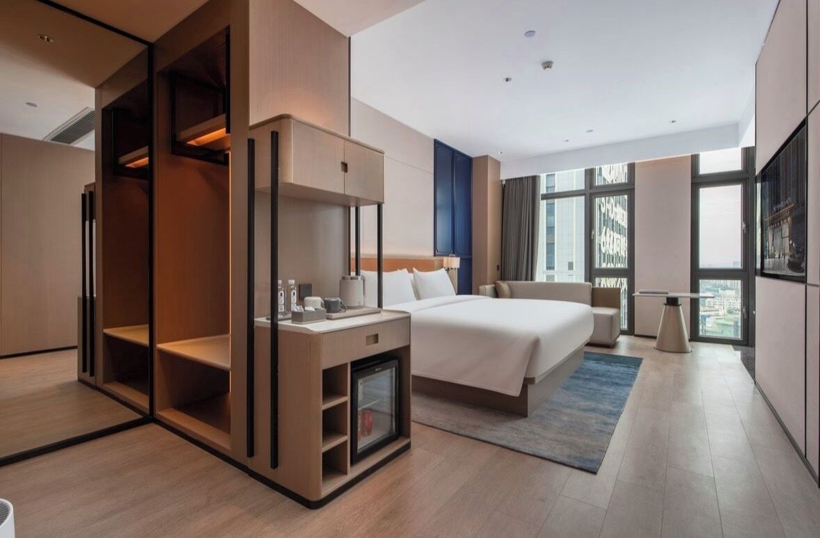 A modern hotel room with a bed, bedside table, and a built-in wardrobe.