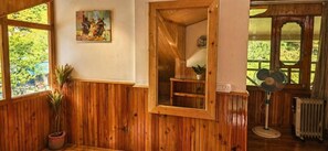 A room with wooden paneling, a potted plant, a painting on the wall, and a fan. - Foresta Living Kasol (Bhuntar)