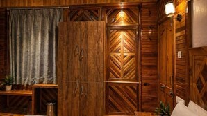 A wooden room with a wardrobe, a shelf with a plant, and a trash bin.
