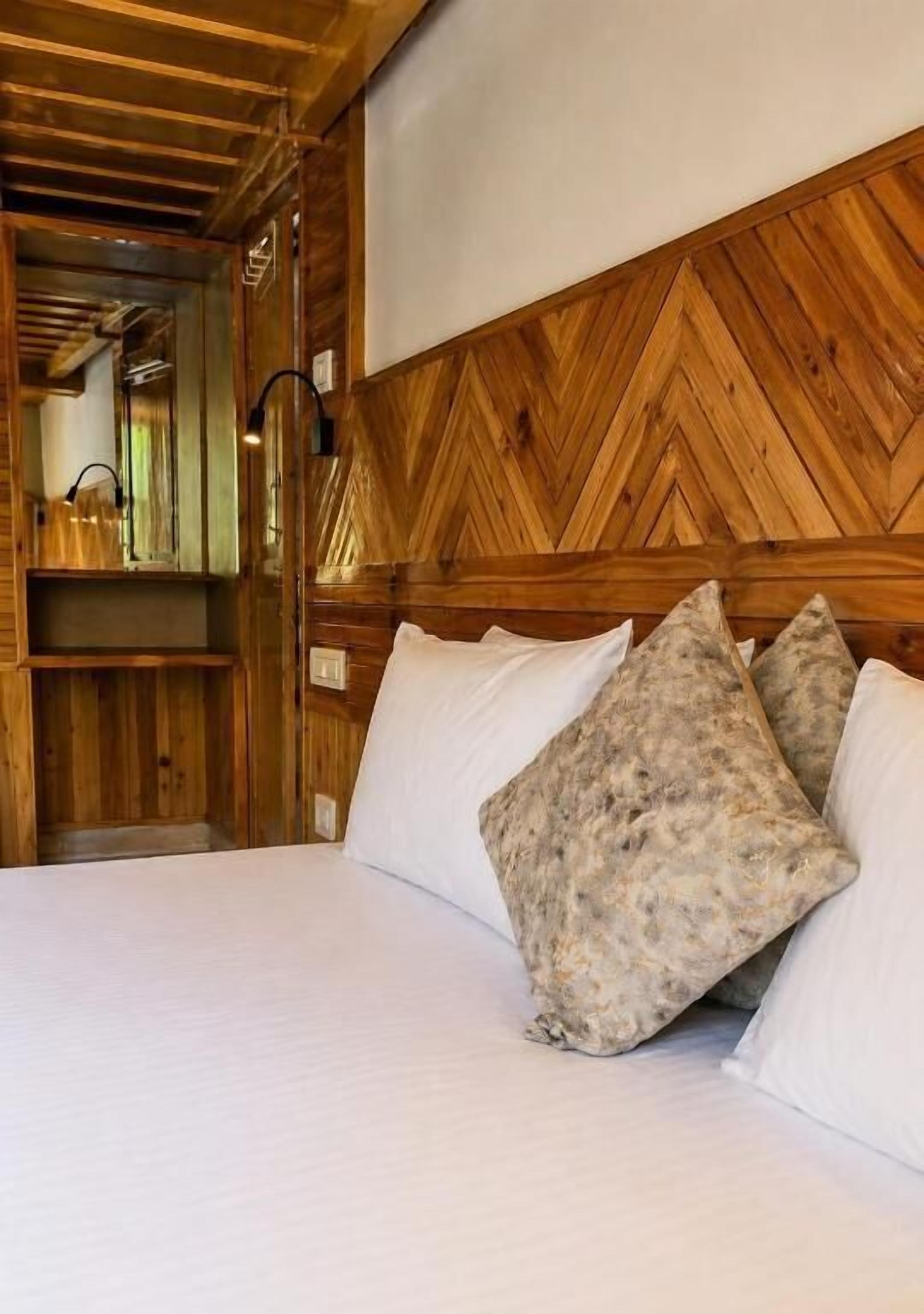Cabecera de madera con diseño en espiga, cama con ropa de cama blanca y dos almohadas con textura.