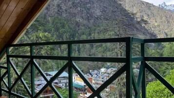 A wooden balcony with a green metal railing overlooking a mountainous landscape.