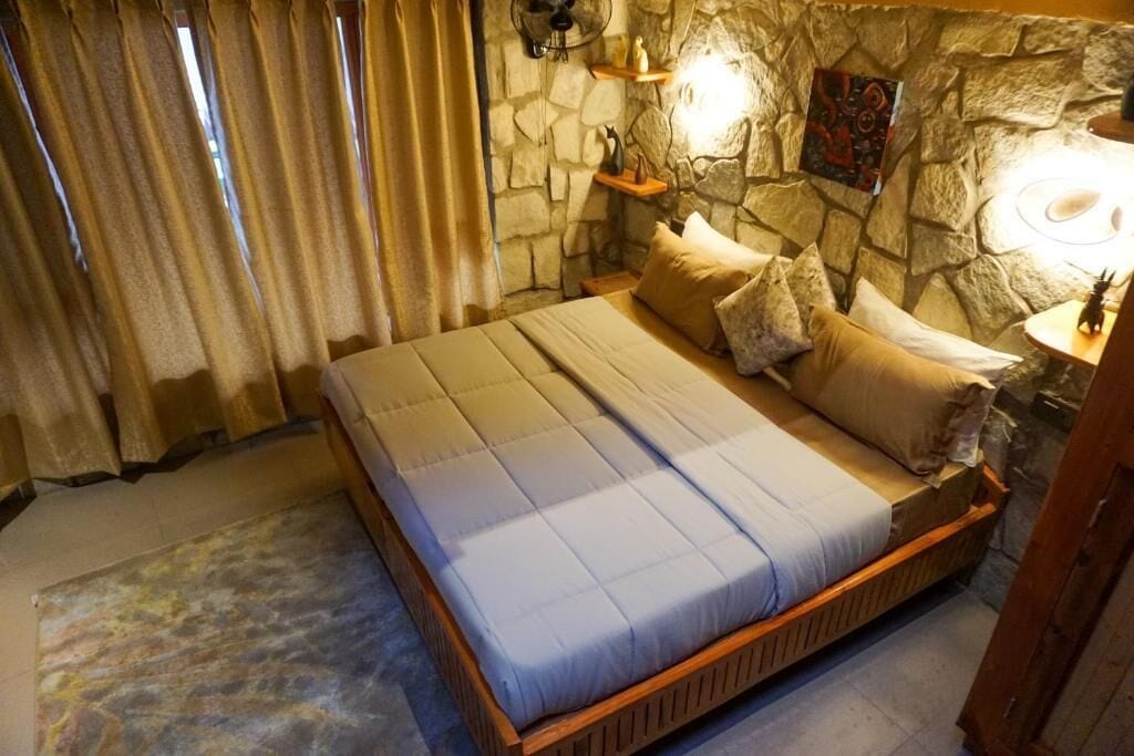 Un dormitorio con pared de piedra, cama con estructura de madera y ventilador de techo.