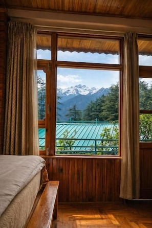 Una habitación con suelo de madera, una cama con cabecero y un ventanal con cortinas.