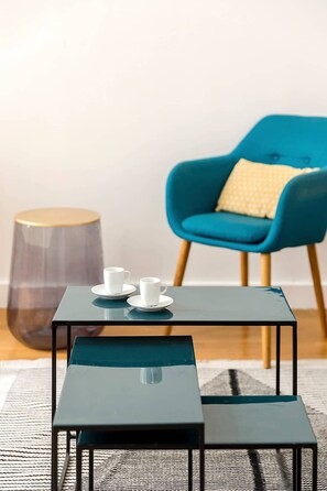 A small, modern room with a dark blue table and bench, two white cups on the table, a blue armchair with a yellow pillow, and a tall, transparent side table. - Elegant apartment near Place Vendôme - 1 bedroom - long stay - Madeleine I by Habitat Parisien (Paris)