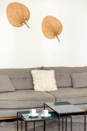A grey sofa with a white fluffy pillow, two white cups on a small table, and two wall-mounted decorative items. - Elegant apartment near Place Vendôme - 1 bedroom - long stay - Madeleine I by Habitat Parisien (Paris)
