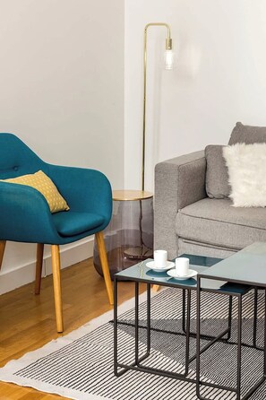 A modern living room with a teal armchair, a grey sofa, a small round side table, and a floor lamp. - Elegant apartment near Place Vendôme - 1 bedroom - long stay - Madeleine I by Habitat Parisien (Paris)