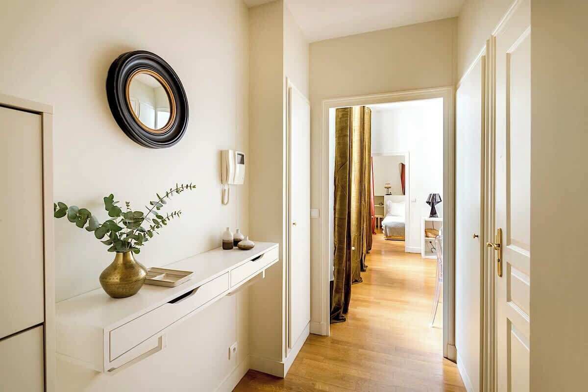 A hallway with a white console table, a mirror, and a vase with green leaves.